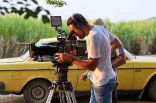 Filming in front of sugarcane and a car.