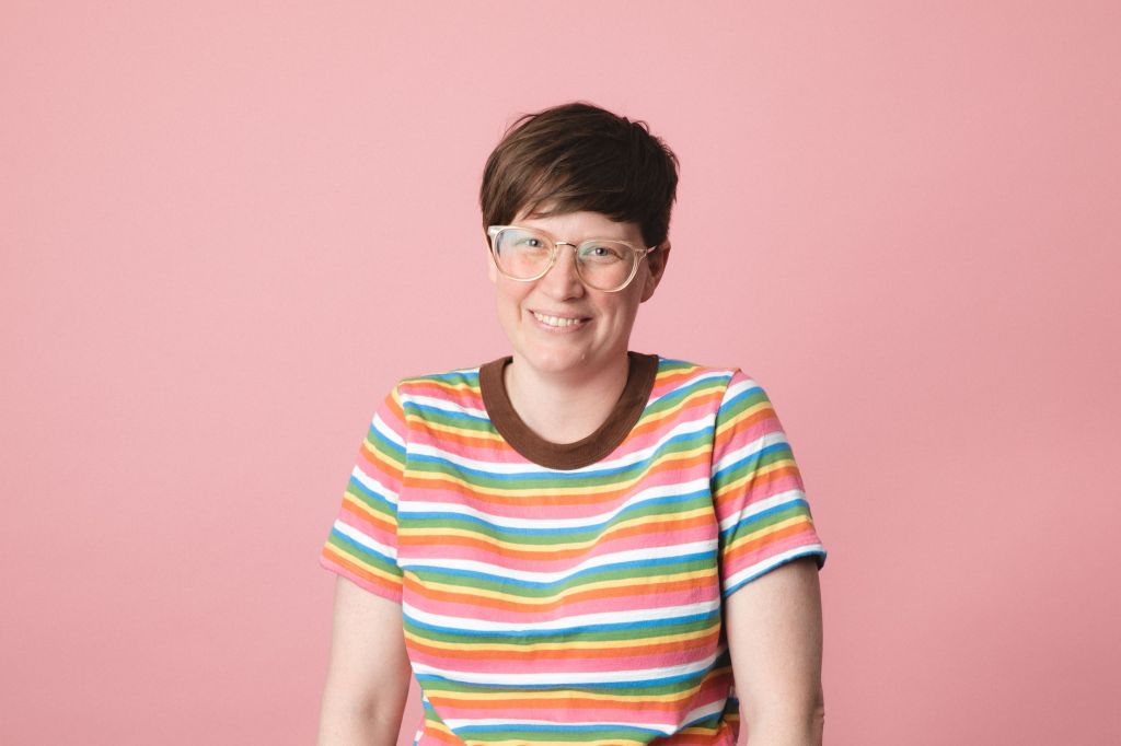 Megan Nairn, League of Geeks' Studio Manager, smiles in front of a pink background
