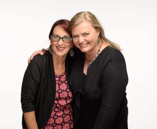 Two women in corporate outfits smiling and hugging