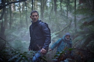 Eric Bana as character Aaron Falk stands in a dense rainforest.