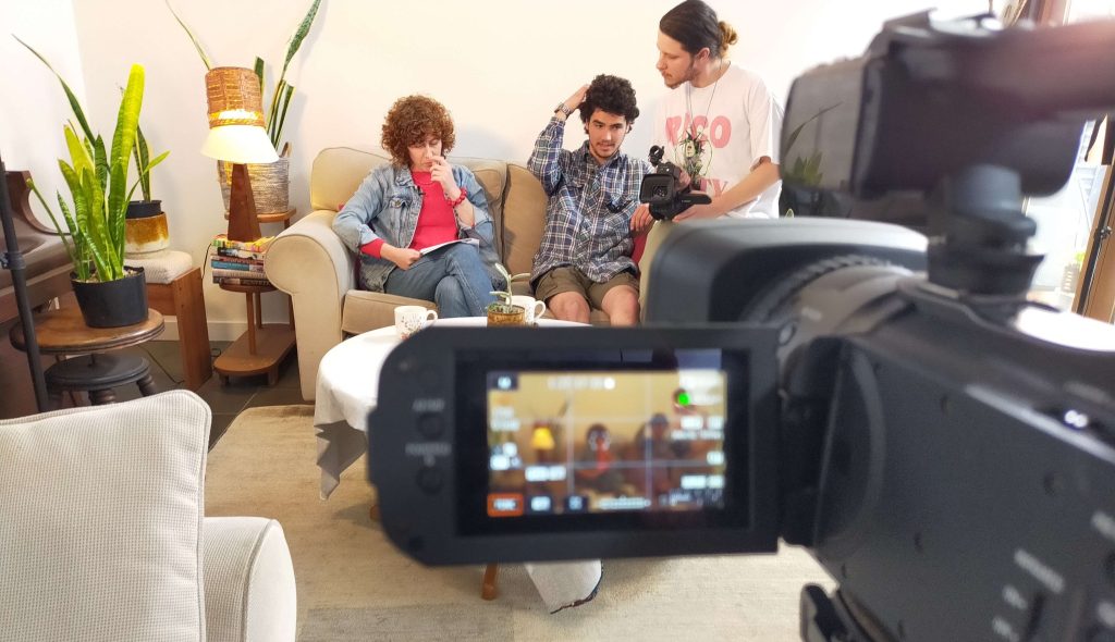 Filmmaking student Felix Wilkins (far right) and two friends sit on a couch and can be seen through a video camera screen in the foreground.