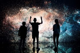 Marshmallow Laser Feast. Image is three silhouettes in front of a large image of a galaxy like world covering an entire wall.