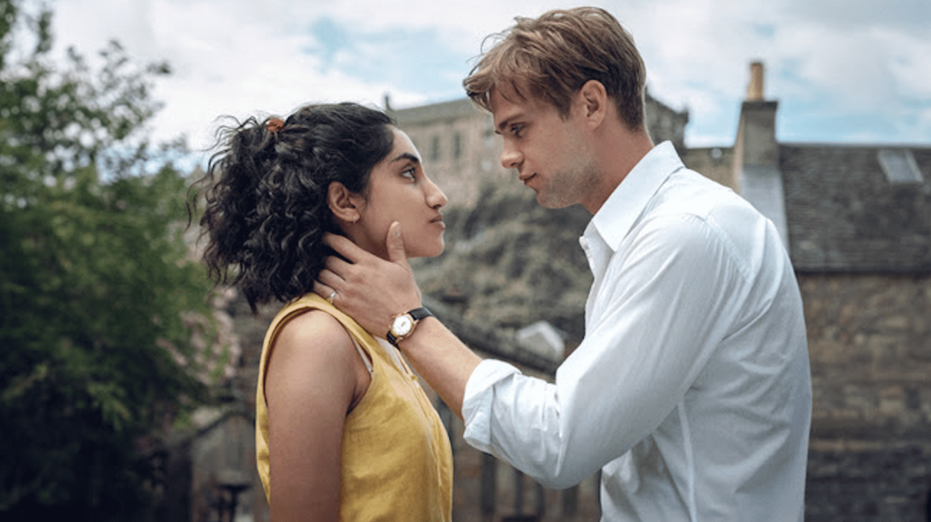 A blonde man in a white shirt looks into the eyes of a brunette woman in a yellow shirt.