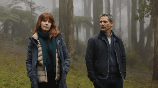 A woman with red hair and a man with grey hair stand in a dense, foggy rainforest.