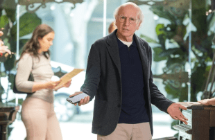 Larry David,a middle-aged man, stands among indoor plants.