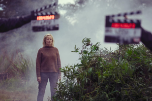 Behind the scenes photo of Bay of Fires. Lead actress Marta Dusseldorp stands between two clapperboards in a foggy bush setting.
