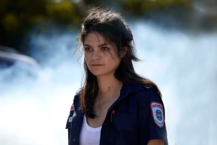 Actress Tahlee Fereday as character Cate, a woman with brunette hair wearing a paramedic's uniform.