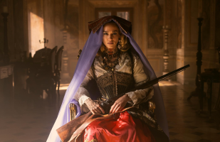 A woman in a red skirt and violet vale with a shotgun on her lap looks directly into the camera in a publicity still for the show Brigands: The Quest for Gold, on Netflix.