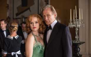 A woman in a green dress and man in a tuxedo look at the camera at a fancy event in a publicity still for Ordeal By Innocence, on BritBox.