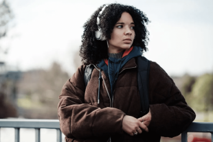 A young woman wearing headphones leans on a railing and looks into the distance in a publicity still for Swift Street on SBS On Demand.