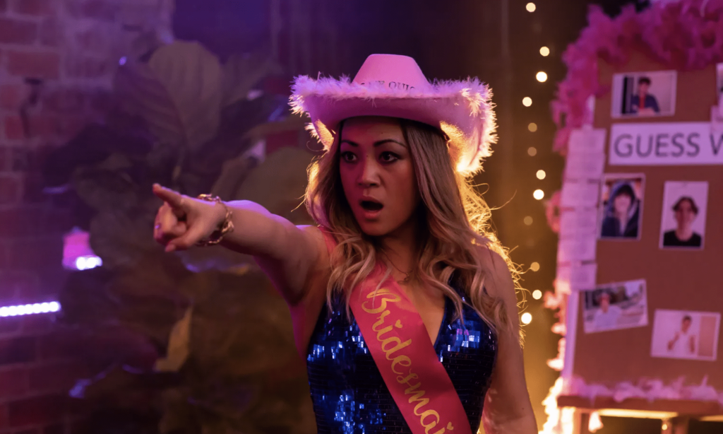 A young woman in a bar with a pink cowboy hat and blue spangly bodysuit, with a pink sash, points into the distance as if choosing something or someone, in a publicity still for White Fever on ABC.