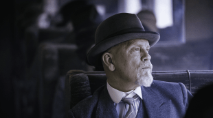 The actor John Malkovich, playing Inspector Poirot, is sitting on a train looking out of the window in a publicity still for Agatha Christie: The ABC Murders on BritBox.