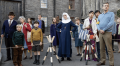 A nun and various other people look out onto a city street in a publicity still for Call the Midwife Season 11 on BritBox.