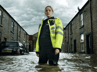 A Woman Police Officer Stands Knee-Deep In Water On A Flooded Street In A Publicity Still For The New Show After The Flood On Britbox.