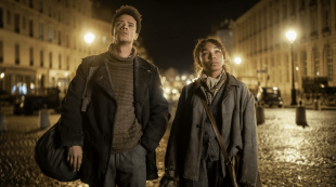 A man and woman walk along a city street at night, lit by lampposts, in a publicity still for Interview With The Vampire Season 2 on AMC+.