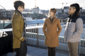 A woman stands between two men on a rooftop having a conversation in a publicity still for Harry Wild Season 3 on AMC+