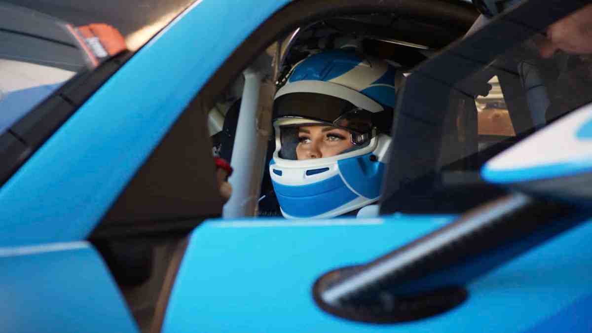 Race driver Renee Gracie sits behind the wheel of a blue race car wearing a blue race helmet in a still from the Stan documentary.