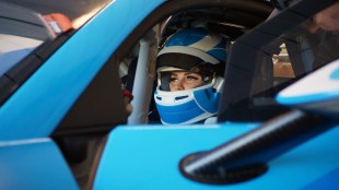 Race driver Renee Gracie sits behind the wheel of a blue race car wearing a blue race helmet in a still from the Stan documentary.