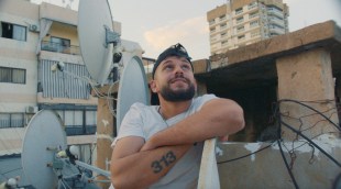 A young bearded man on a rooftop looks into the sky in a still from the documentary Kash Kash on DocPlay.