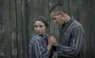 A woman and a man, both prisoners, hold hands, wearing concentration camp uniforms, in a still from The Tattooist of Auschwitz on Stan.