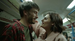 A smiling woman gets close to a smiling but nervous-looking man's face on public transport, IN Baby reindeer on Netflix.