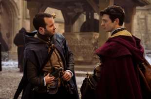 Two young men in Tudor garb face each other with quizzical looks in a courtyard, in a still from Shardlake on Disney+.