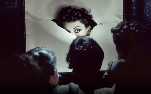 Three people face towards a screen on which an evocative image of a woman is displayed.
