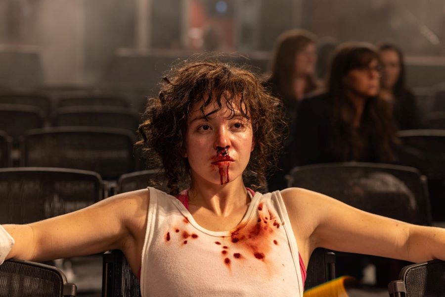 The Titular Character In Boxing Biopic Christy Sits In Ringside Seats, Her Nose And White Singlet Bloodied.