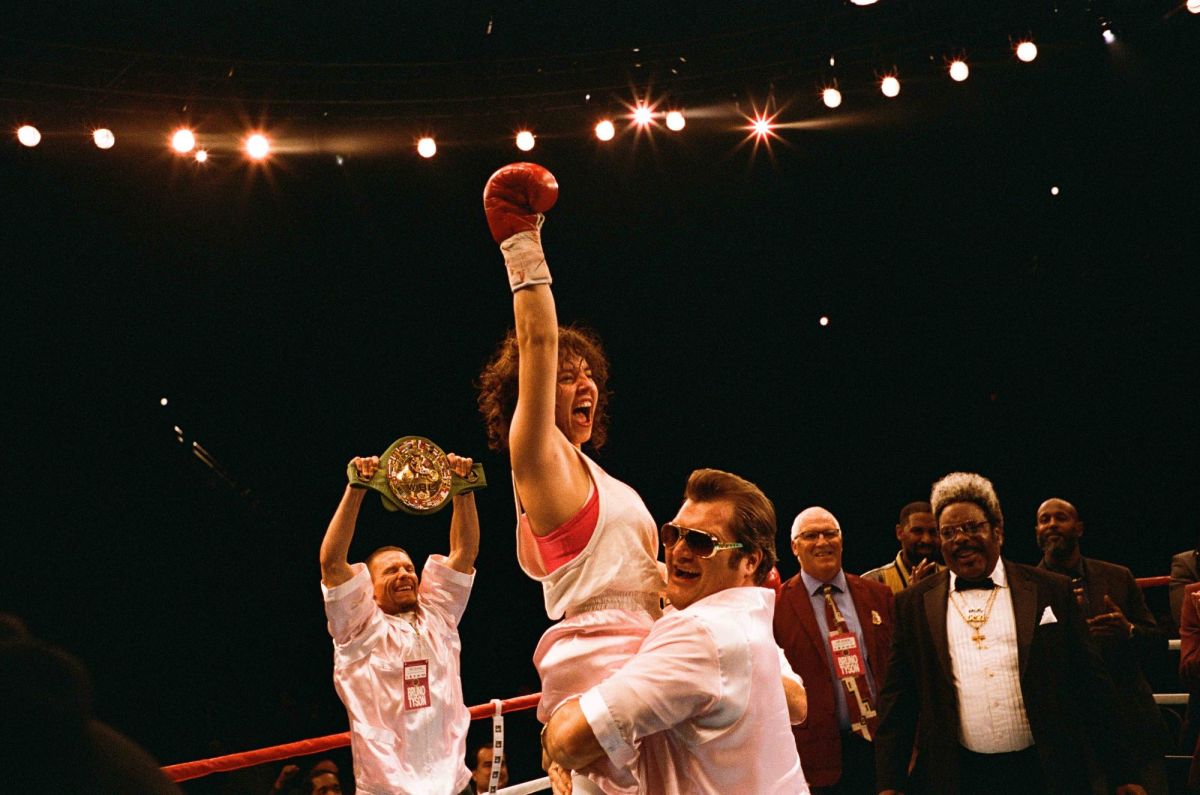 A scene from boxing biopic Christy showing Sydney Sweeney as the title character, gloved fist triumphantly raised as a man hoists her aloft in the boxing ring. Other men look on.