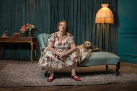 Dr Jeni Haynes lives with dissociative identity disorder, and is the subject of the compelling new SBS-screened documentary We Are Jeni. A middle-aged woman wearing a floral dress and glasses sits on a chaise lounge next to a small brown dog.